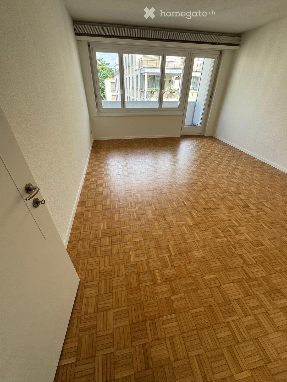 large window with balcony, wooden parquet flooring, white walls