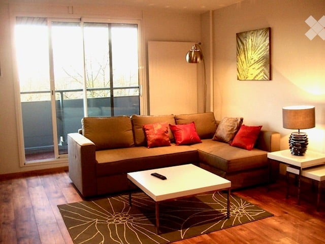 Living Room. Modern living room with a sectional sofa, coffee table, side table, floor lamp, and a picture frame on the wall. Large windows with a balcony view.