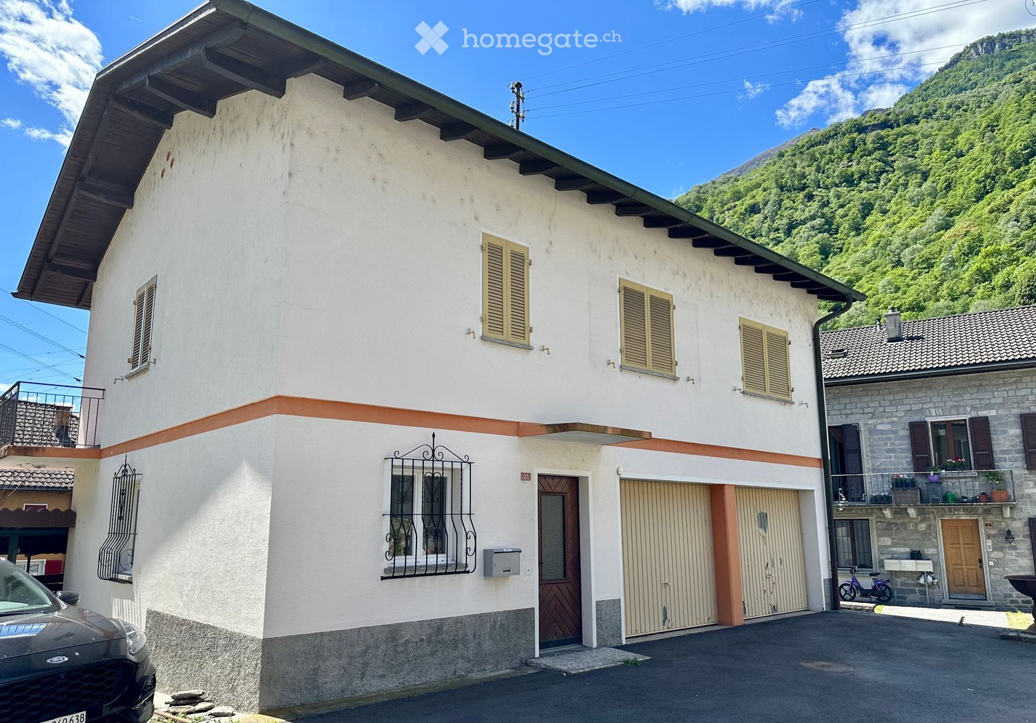 House. Two-story white house with wooden shutters, garage, and balcony overlooking a mountainous landscape.