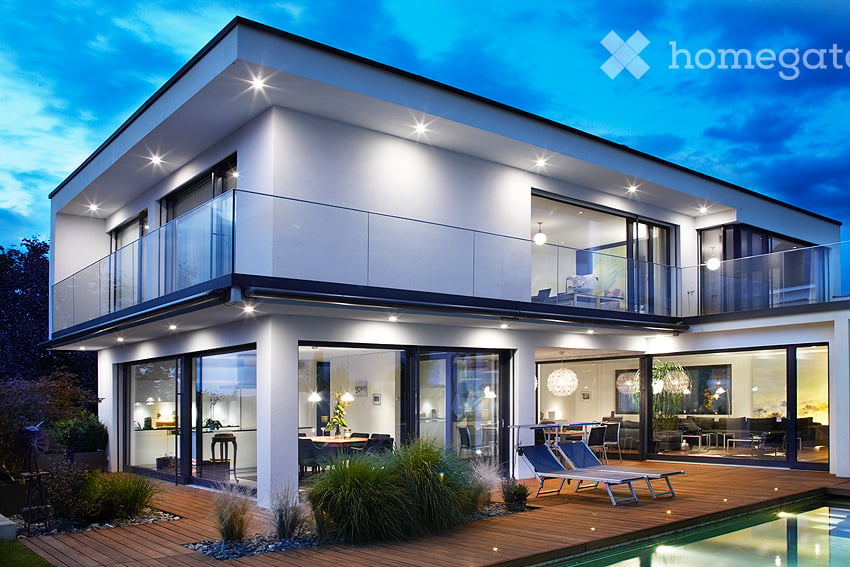 Building. Modern two-story house with large glass windows and a balcony, featuring a swimming pool and outdoor seating area.