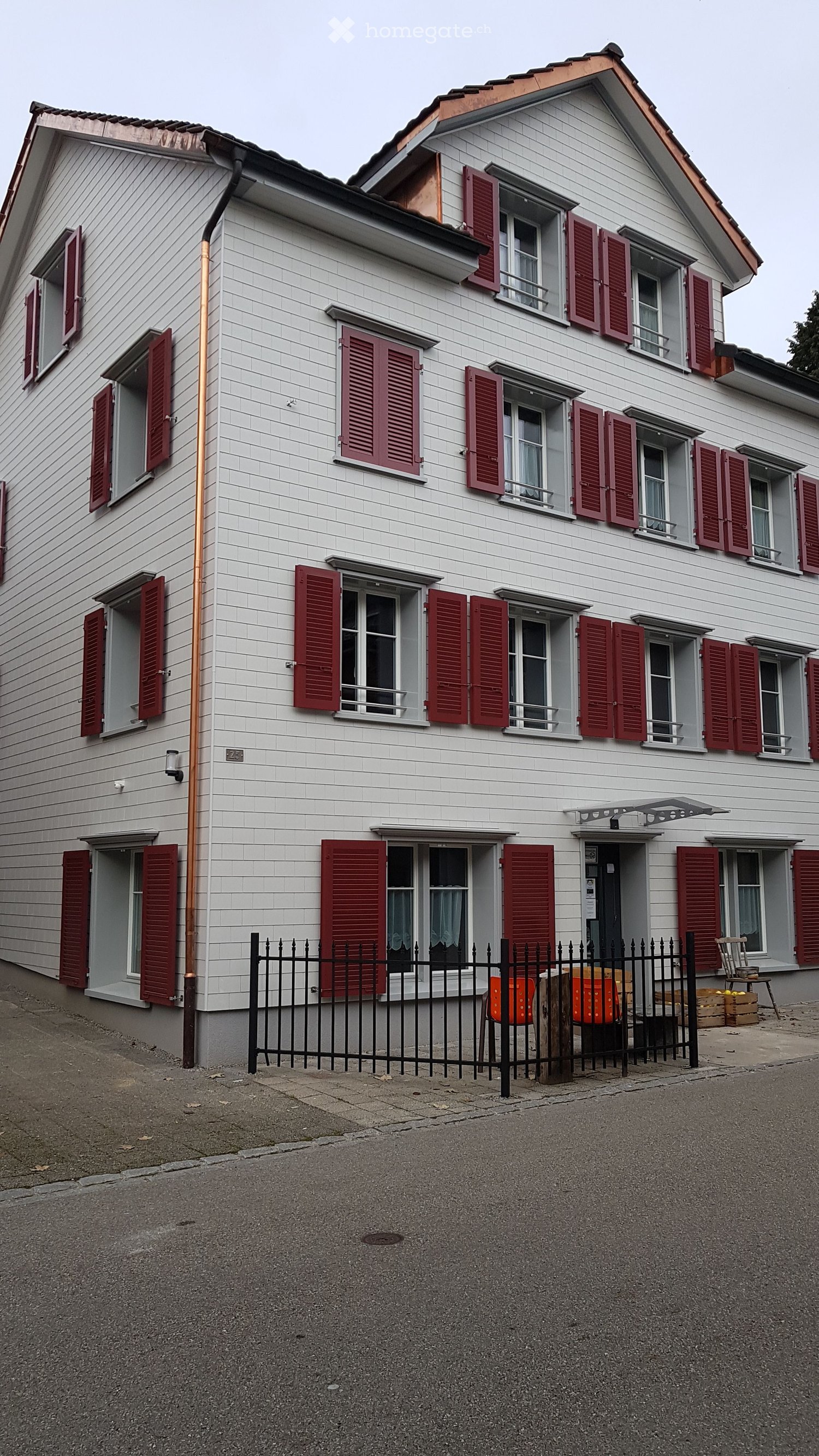 House. Two-story house with white siding, red shutters, multiple windows, and a small fenced front yard.