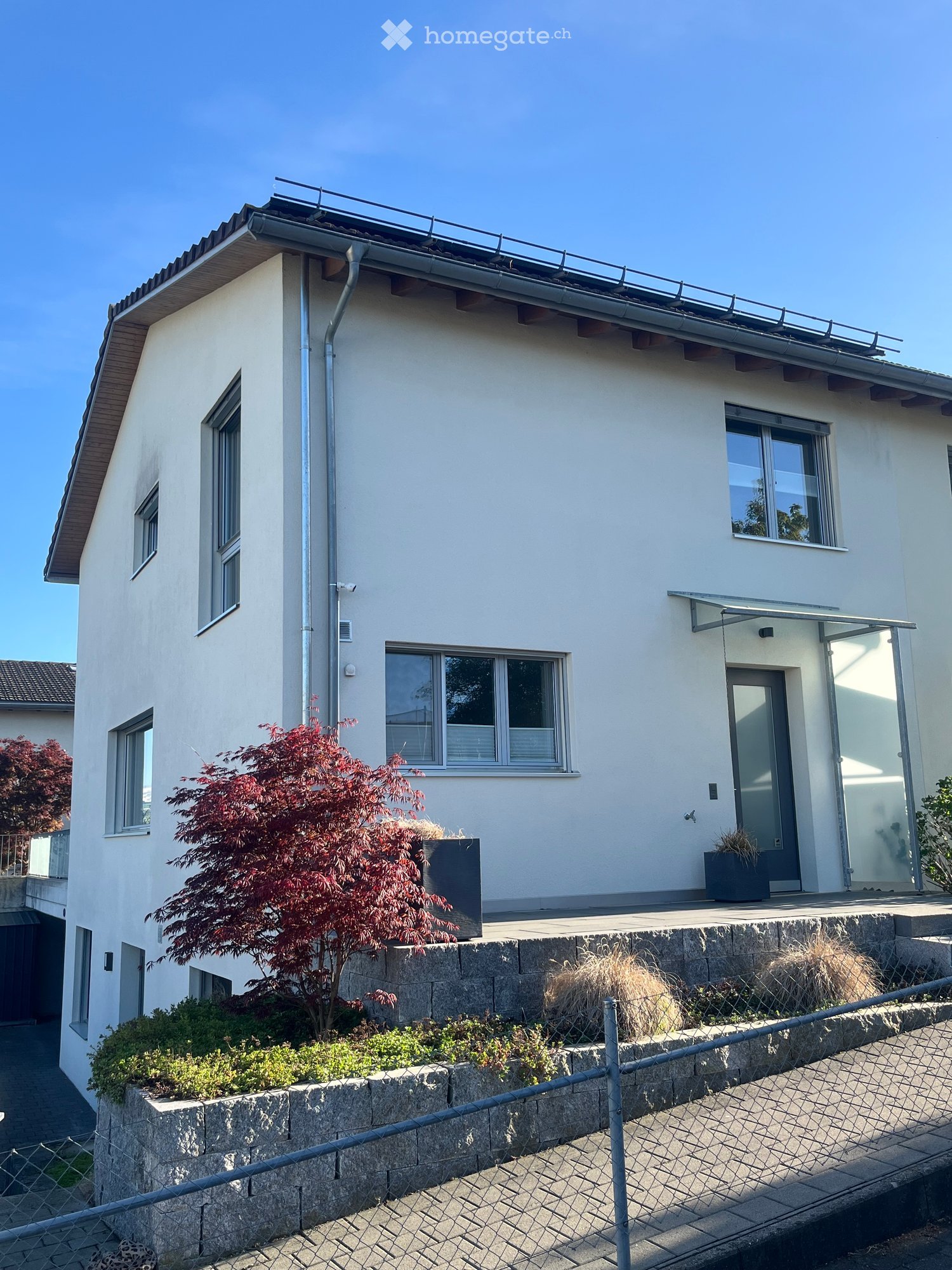 House. Modern two-story house with white exterior, multiple windows, and a small balcony area with potted plants.
