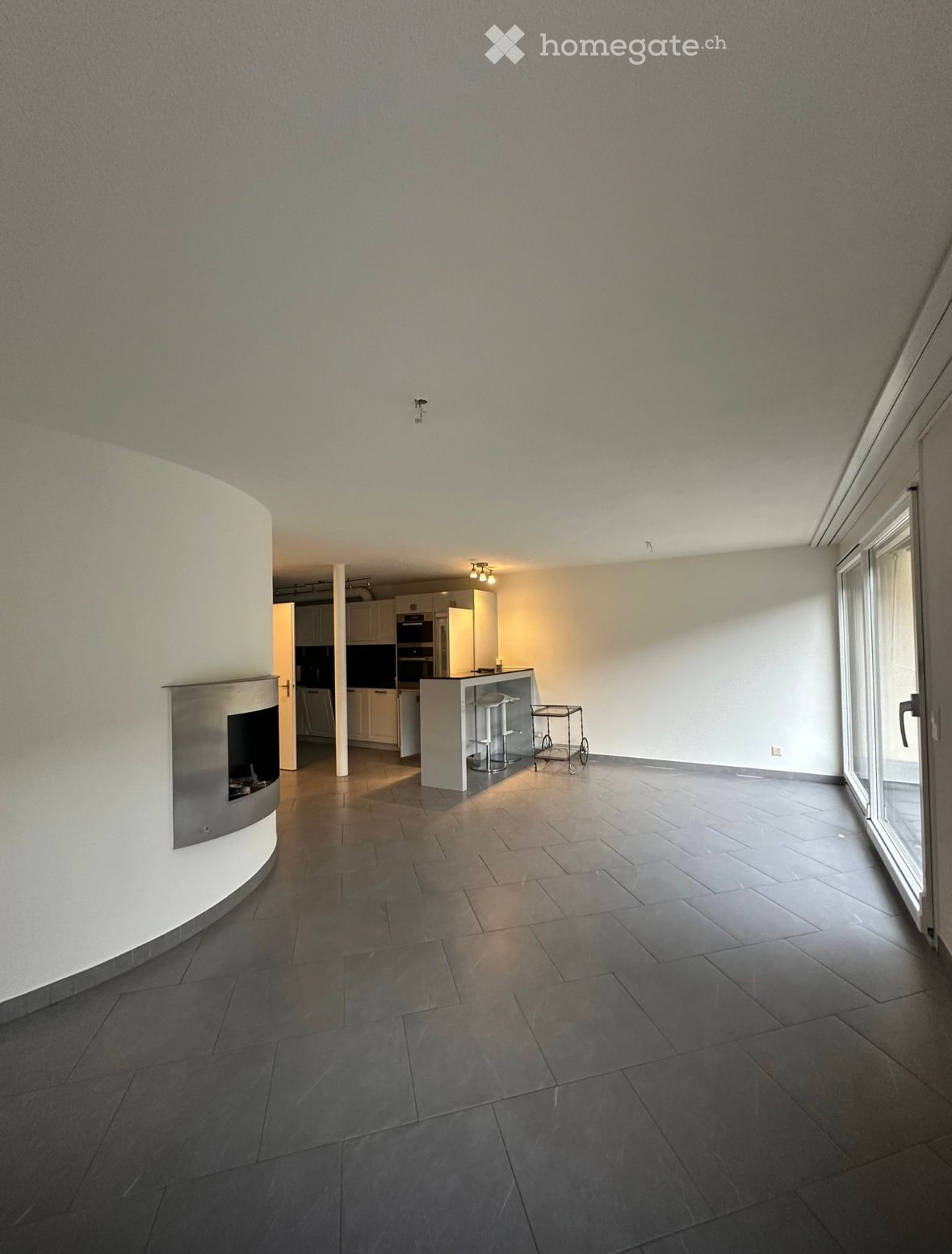 empty room with white walls, fireplace, sliding glass door, kitchen with appliances and stools