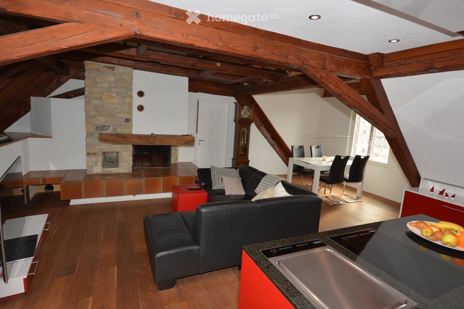Open-plan living and dining area with wooden beams, fireplace, leather sofa, dining table, and modern kitchen island.