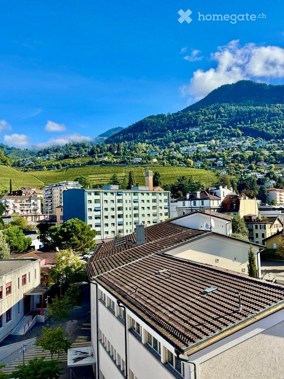 Aerial view of a town with multiple buildings, green hills, and a clear blue sky
