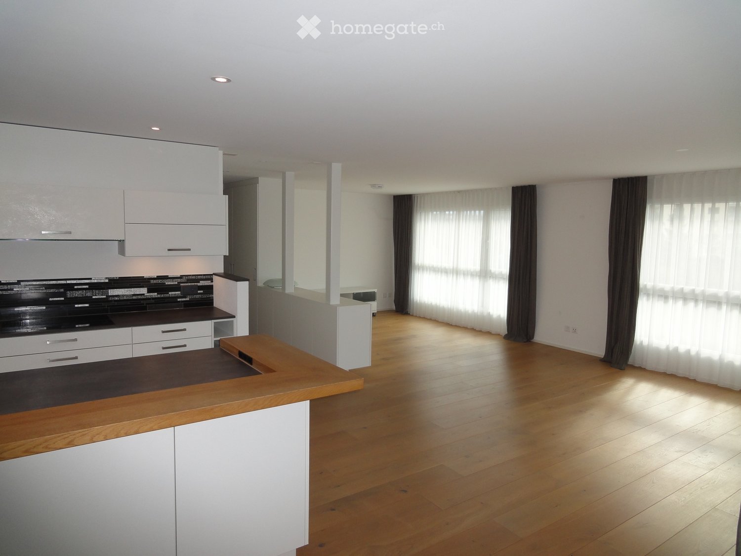 Furnished Room. Modern kitchen with white cabinets, dark countertops, and a wooden island. Large windows with curtains let in natural light.