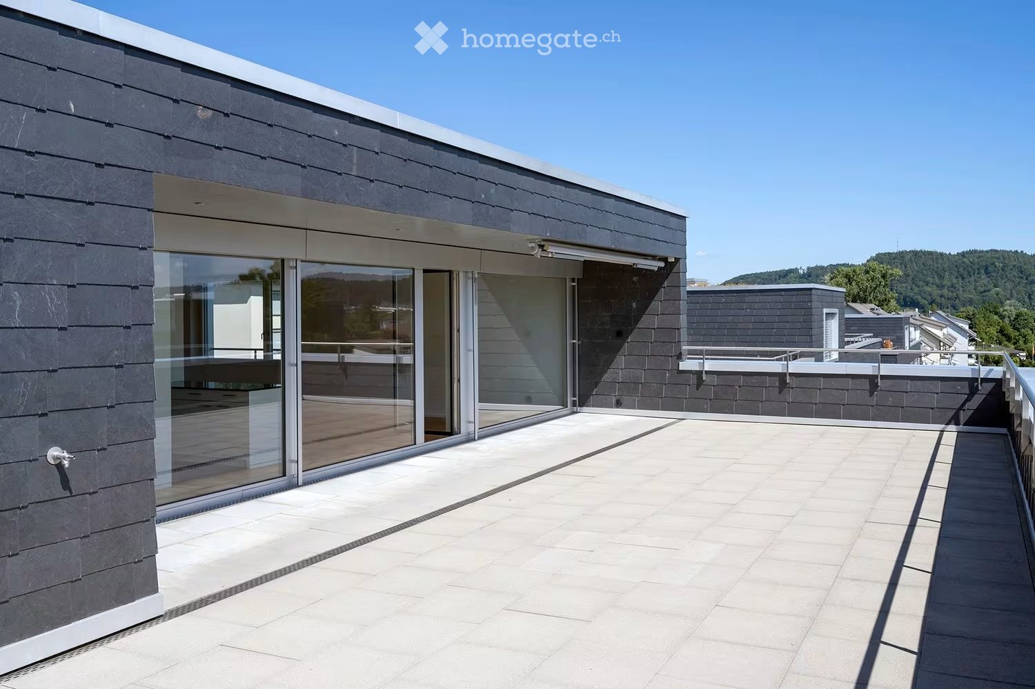 Balcony / Terrace. Modern rooftop terrace with large glass sliding doors, white tiled flooring, and a view of the surrounding landscape.