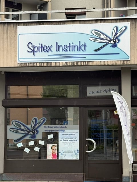 Building. Storefront with a sign reading "Spitex Institut" and a dragonfly logo. The entrance features glass doors with promotional posters and a banner visible outside.