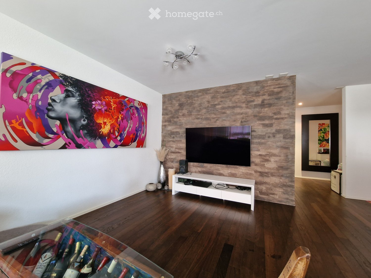 Living room with wooden floor, large colorful painting, flat screen TV, white entertainment center, decorative items