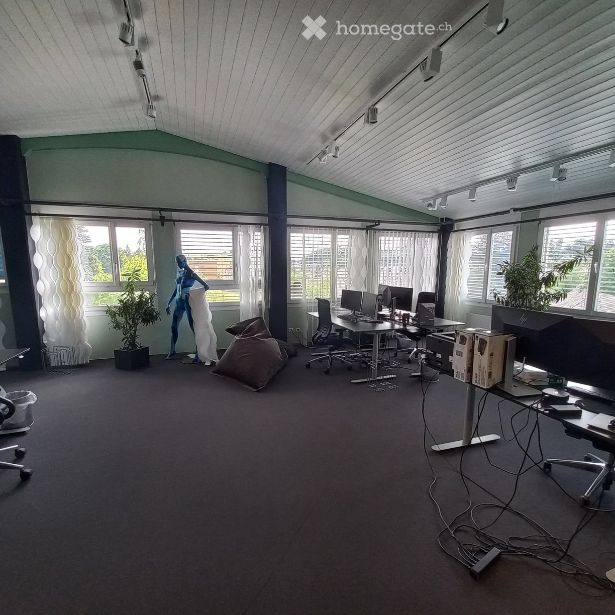 Furnished Room. Office space with multiple desks, chairs, computer monitors, and a plant. The room has large windows with blinds and a modern, open layout.