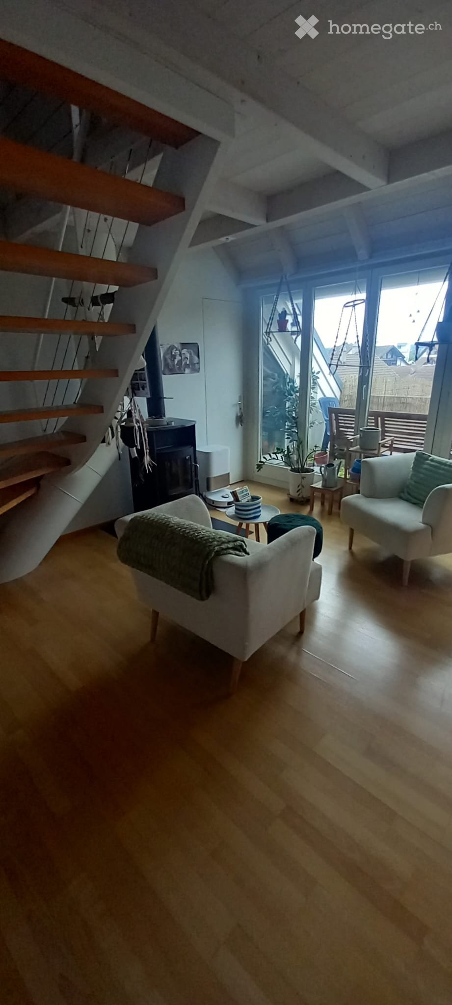 Living Room. Modern living room with wooden flooring, a fireplace, and large windows offering a view. Features include a sofa, chairs, coffee tables, and a staircase leading upwards.