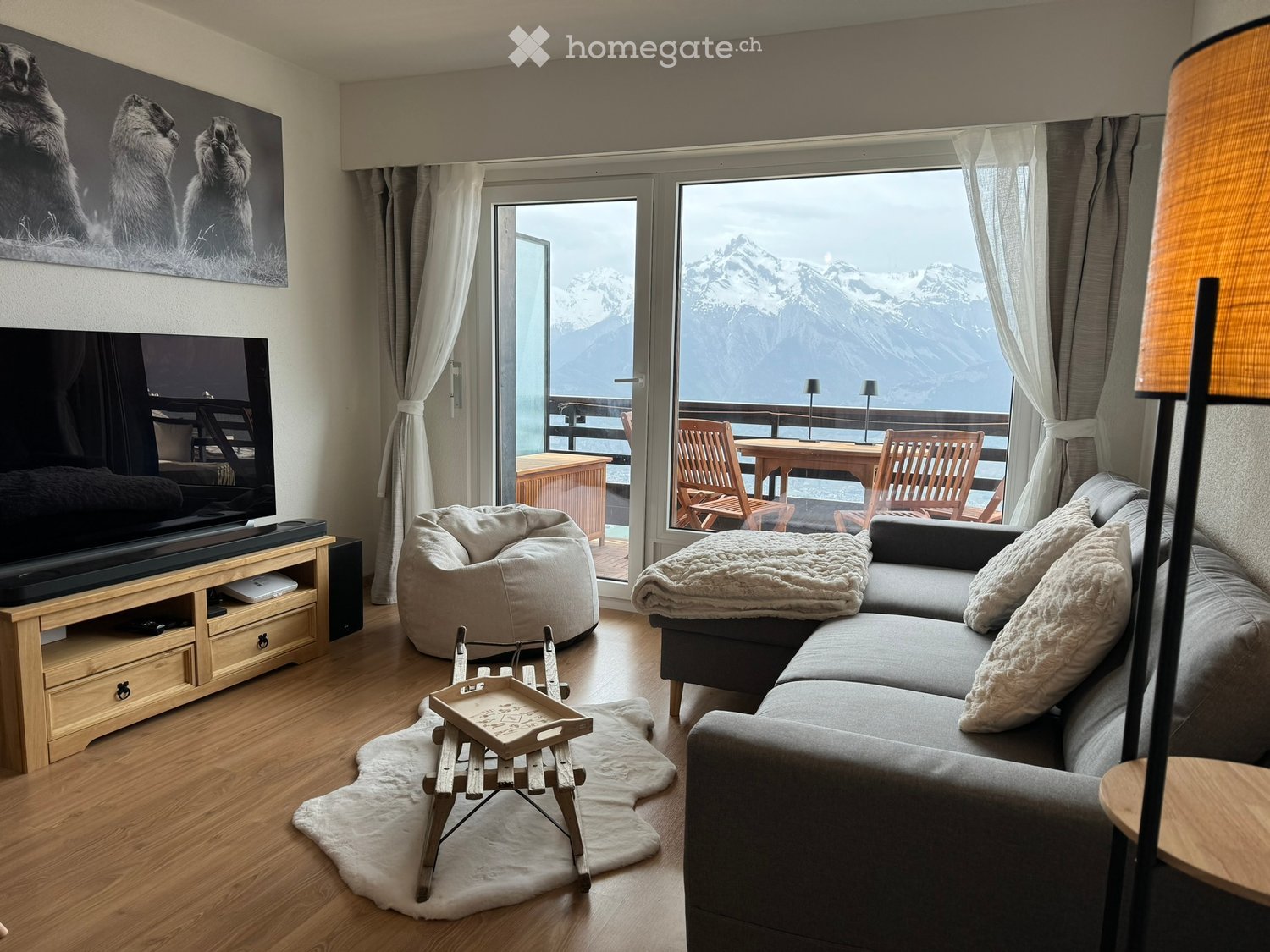 Living Room. Modern living room with a large window offering a mountain view, featuring a grey sectional sofa, a bean bag chair, a coffee table, a television, and a floor lamp.