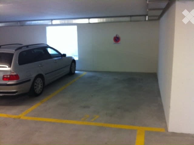 Building. Underground parking area with one parked car, marked parking spaces, and a large window allowing natural light.