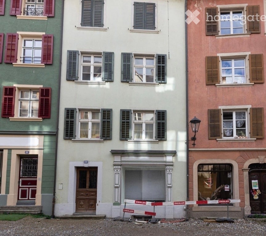 Building. Three-story residential building with classic European architecture, featuring multiple windows with shutters, a central entrance with ornate columns, and adjacent buildings with varied facades.
