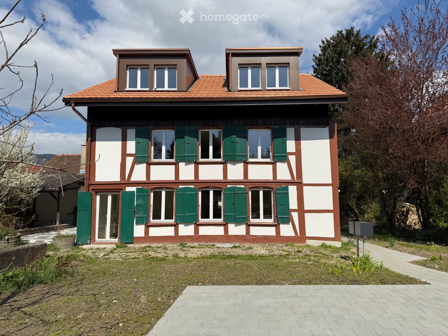 House. Two-story house with white and brown exterior, green shutters, red-tiled roof, and multiple windows.