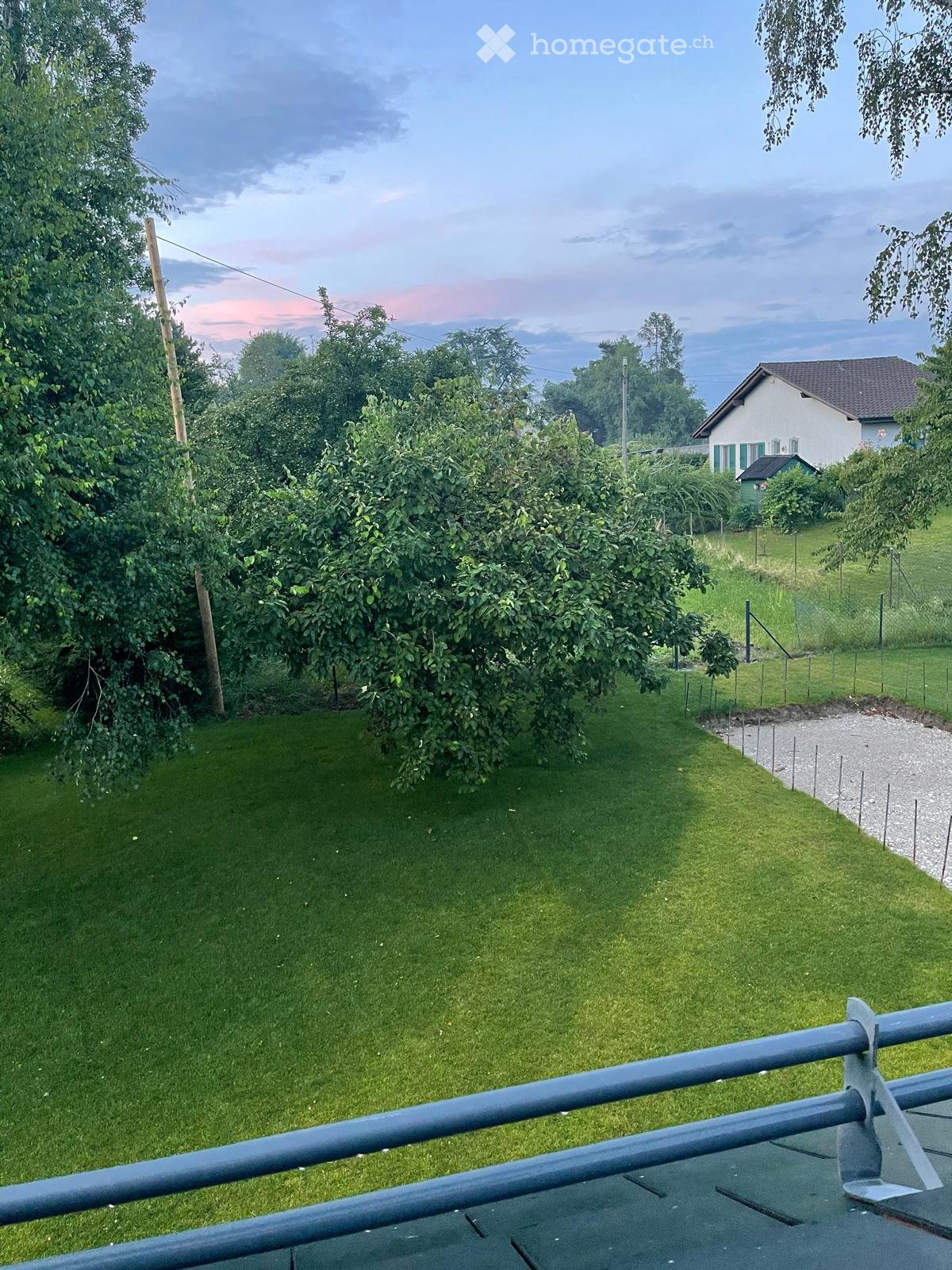 Garden / Outdoor Area. A well-maintained garden with a lawn, trees, and a small house in the background.