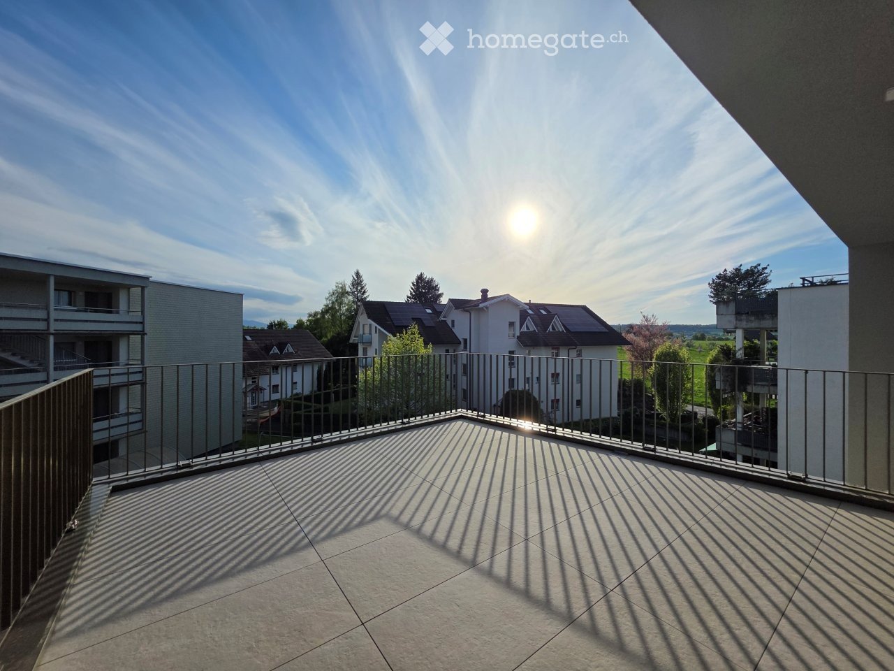 Balcony / Terrace. Balcony with metal railing, tiled floor, and view of surrounding buildings and greenery.
