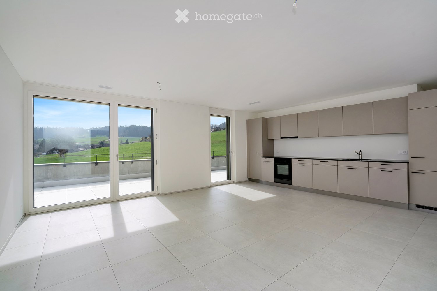 Kitchen. Modern, minimalist kitchen with light grey cabinets, a central island, and large windows offering a scenic view of green fields.