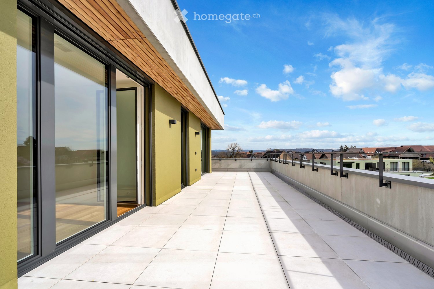 Balcony / Terrace. Modern rooftop terrace with white tiled flooring, glass sliding doors, wooden roof overhang, and a view of the surrounding area.