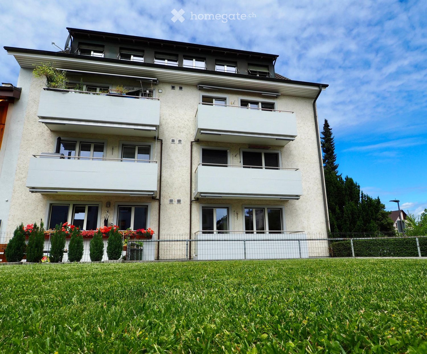 Building. Modern three-story apartment building with multiple balconies, white exterior, and well-maintained garden area in front.