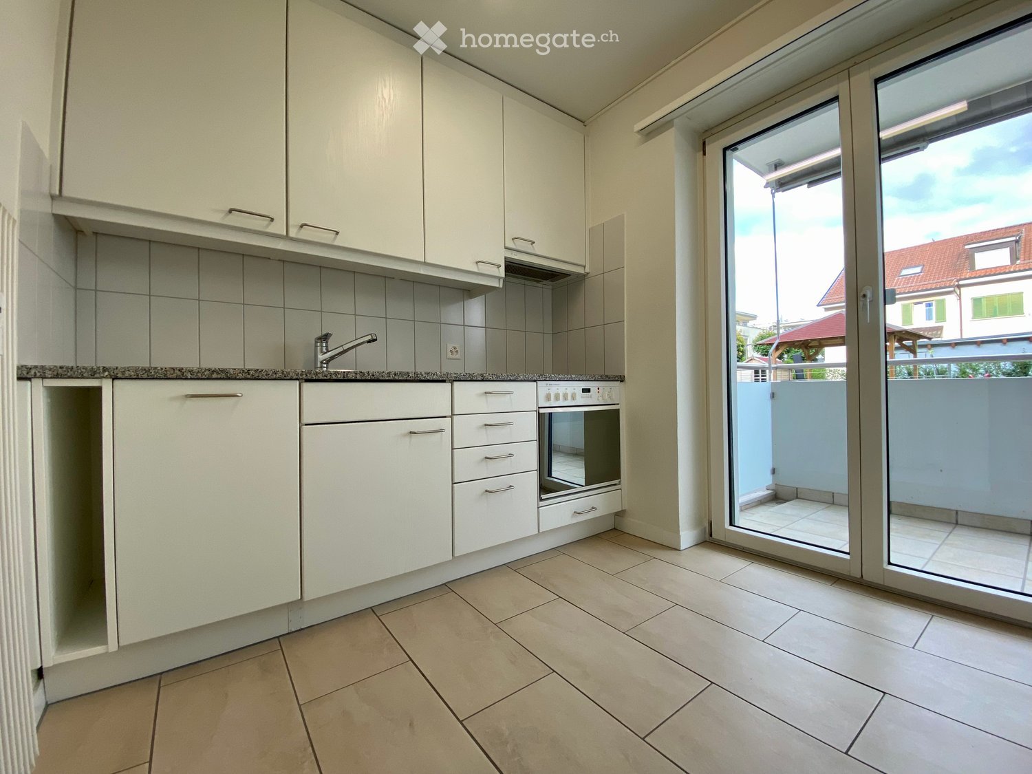 Kitchen. Modern kitchen with white cabinets, tiled backsplash, granite countertop, and an open sliding door leading to a balcony.