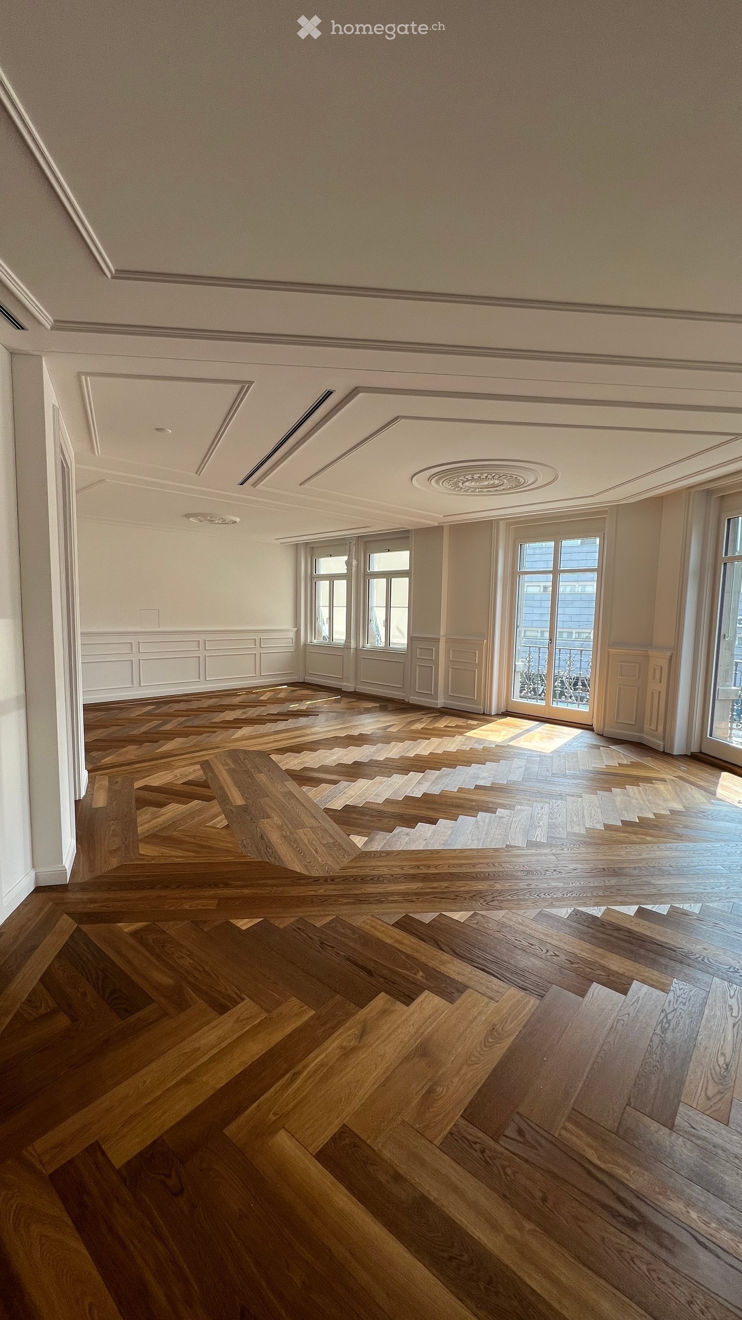 Unfurnished Room. Empty room with wooden herringbone flooring, white walls, large windows, and decorative ceiling moldings.