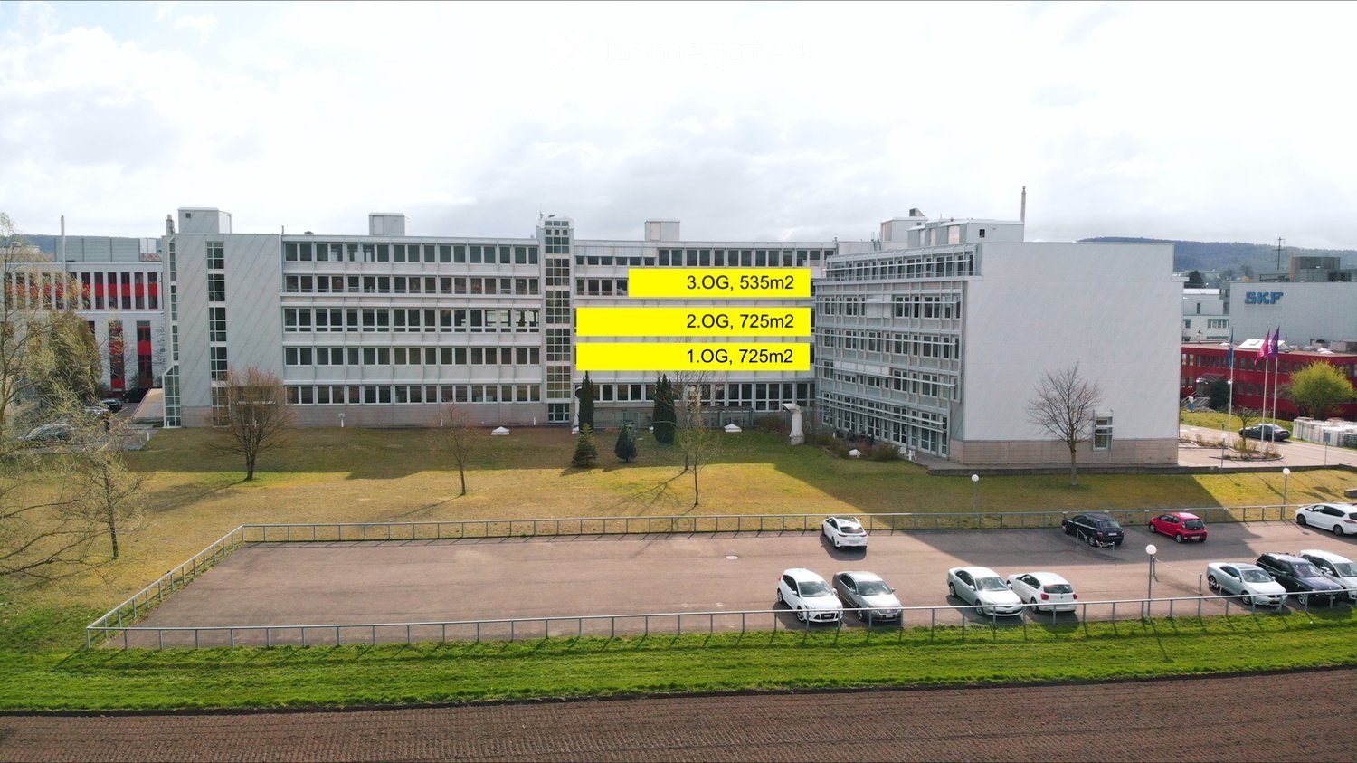 3 floors, white structure, glass windows, surrounding greenery, multiple cars parked