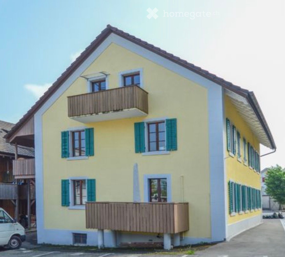 House. Two-story yellow house with green shutters, multiple windows, and two balconies on the upper floor.