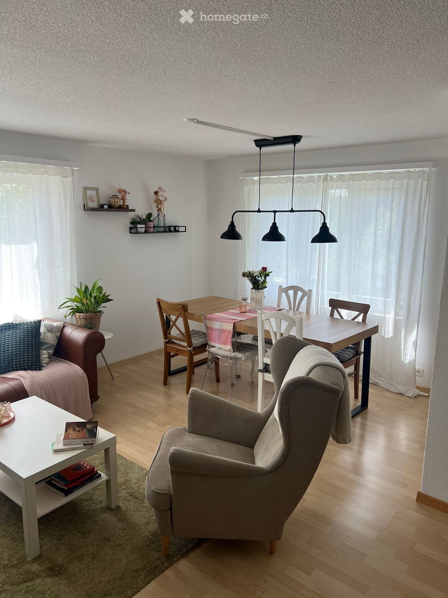 Furnished Room. A modern living room with a sofa, armchair, coffee table, dining table, chairs, and decorative items including plants and books.