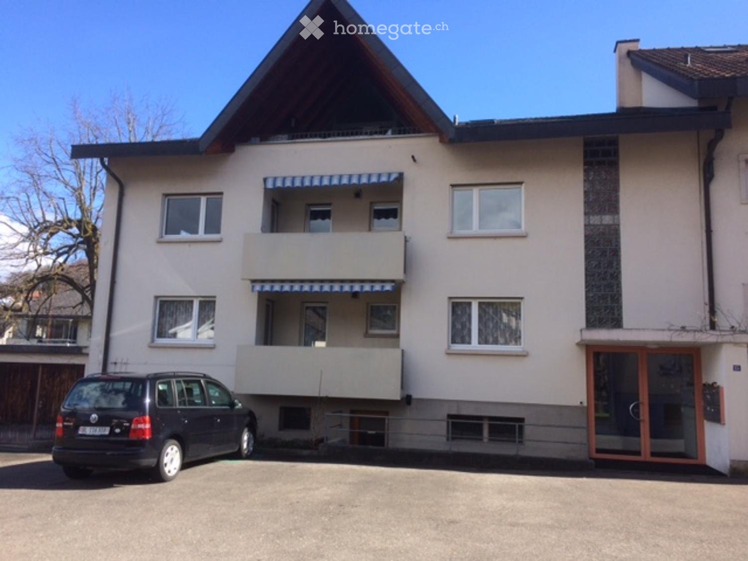 House. Two-story house with light beige exterior, multiple windows, balconies, and a parked car in front.