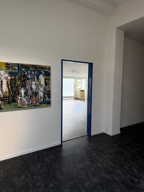 Unfurnished Room. Empty room with dark flooring, white walls, and a large abstract painting on one wall. A doorway leads to another room with light-colored furniture visible.
