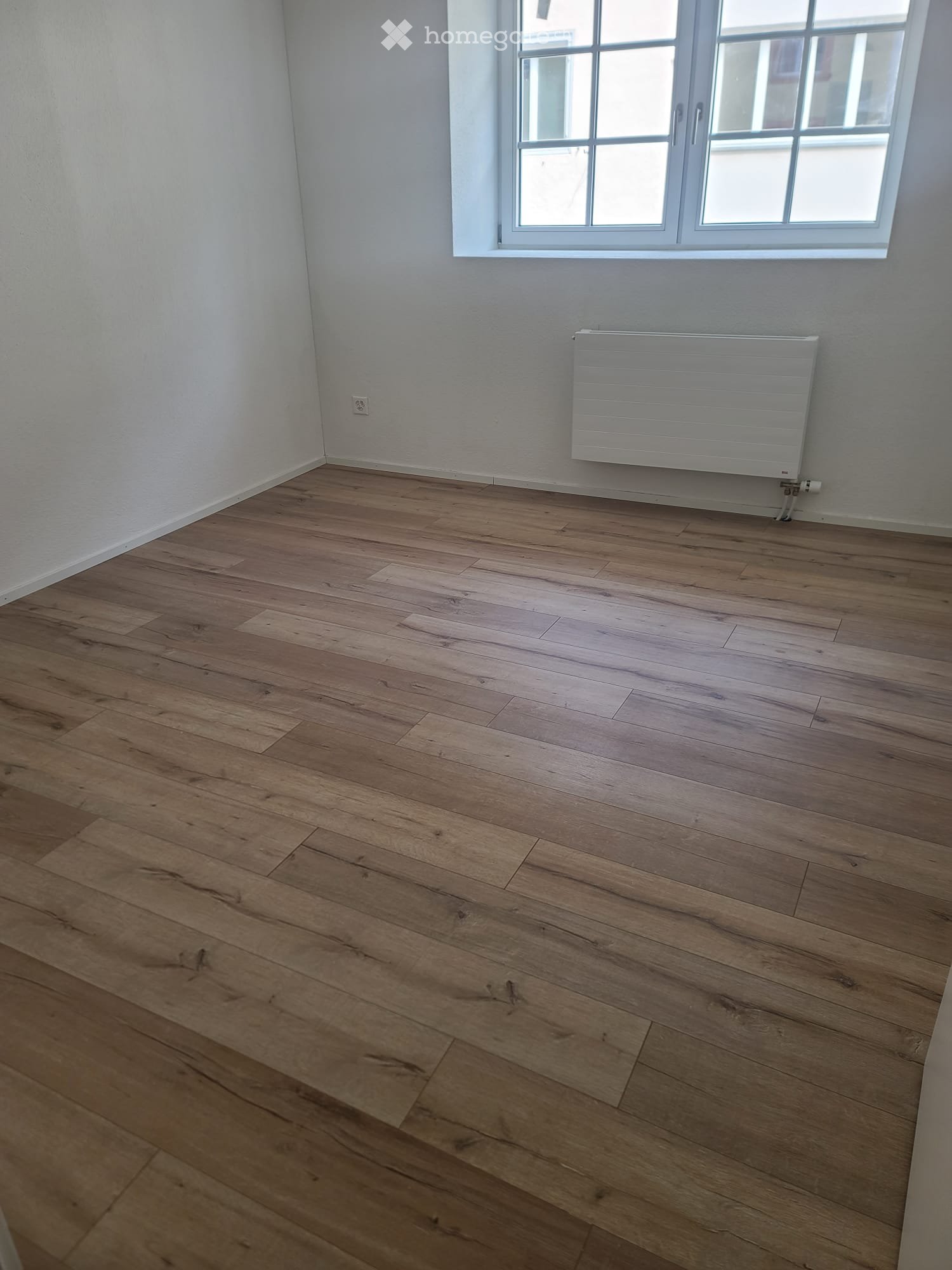 Unfurnished Room. Empty room with wooden flooring, white walls, a window, and a radiator.