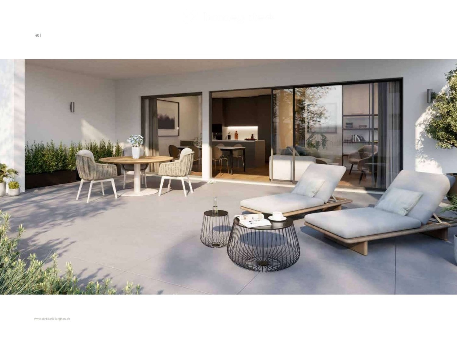 Garden / Outdoor Area. Modern outdoor patio with a round dining table, wicker chairs, two lounge chairs, small metal stools, and a cup on one of the stools. The area is surrounded by greenery and has large glass doors leading to an indoor space.
