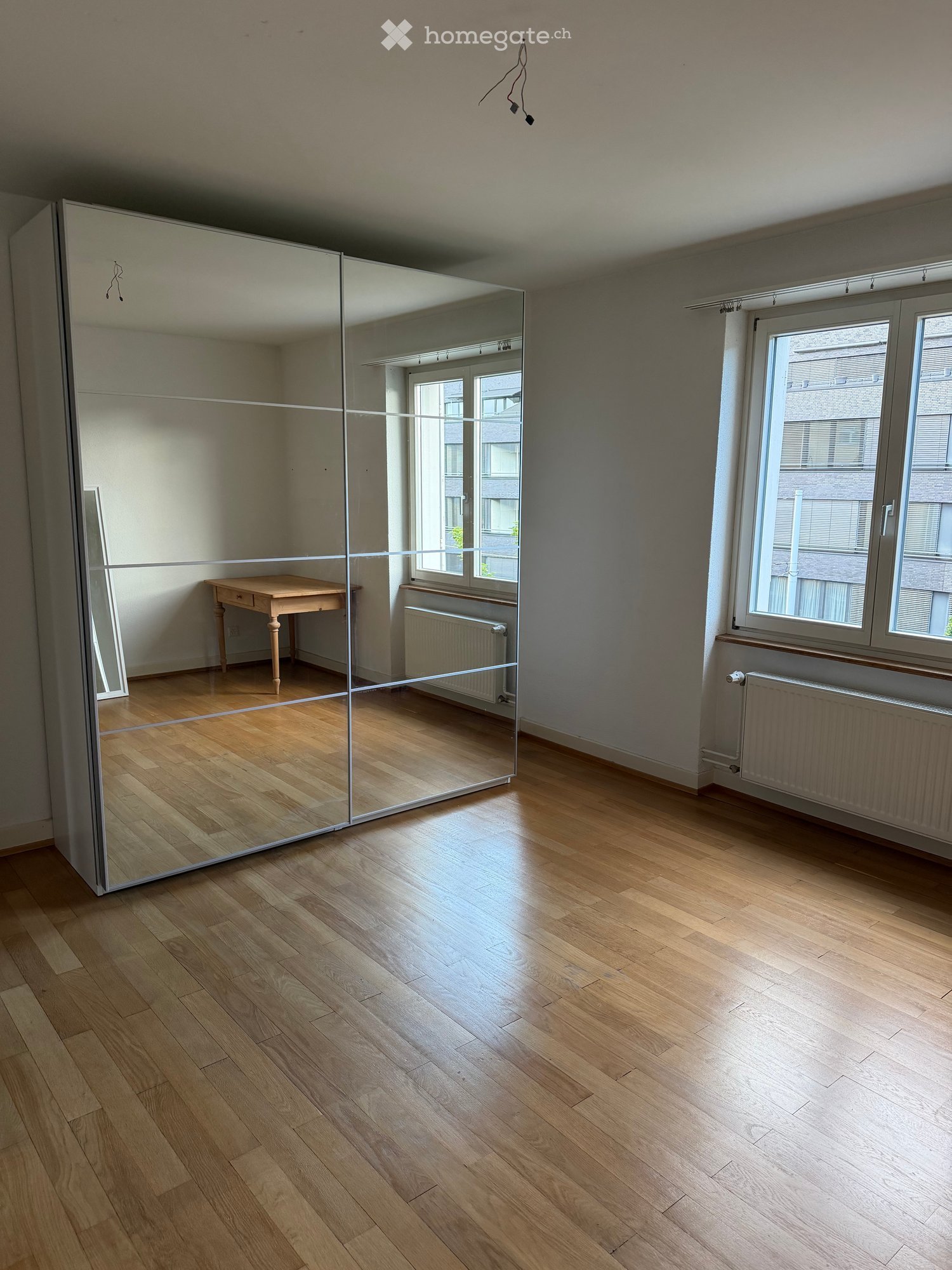 Empty room with wooden flooring, large mirrored wardrobe, small wooden table, and windows with radiators.