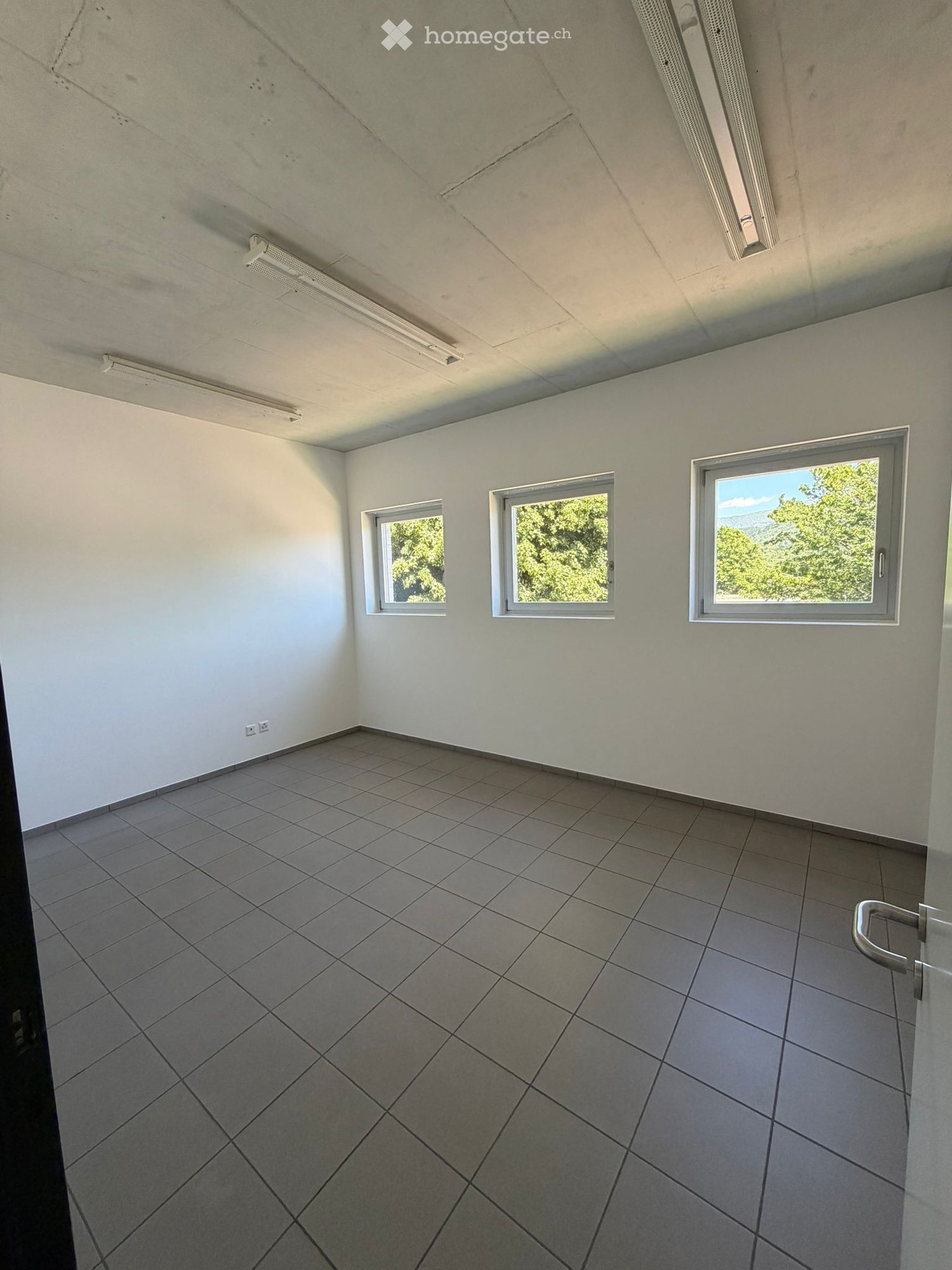 Unfurnished Room. Empty room with white walls, tiled floor, and three windows offering a view of greenery.
