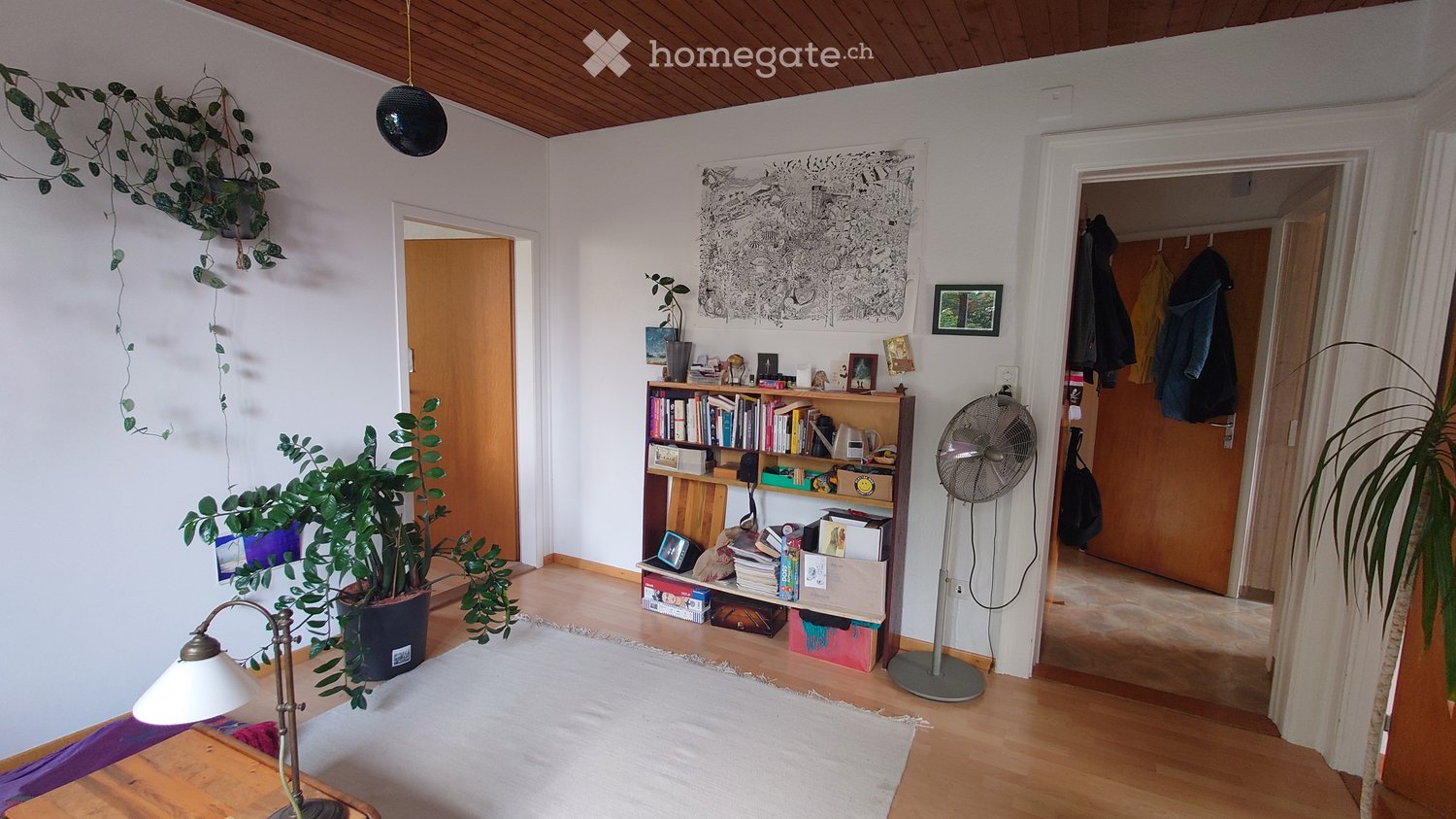 wooden floor, white walls, various plants, bookshelf with books, fan, rug, hanging lamps