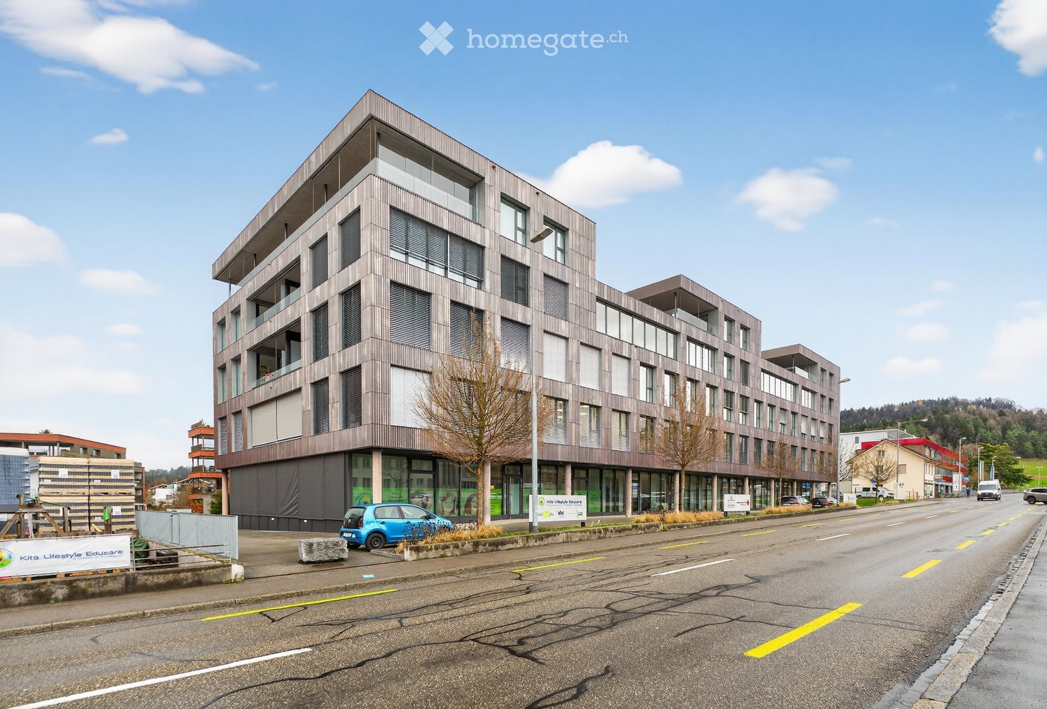 Modern residential building with many windows, located on a street, gray exterior, multiple cars parked
