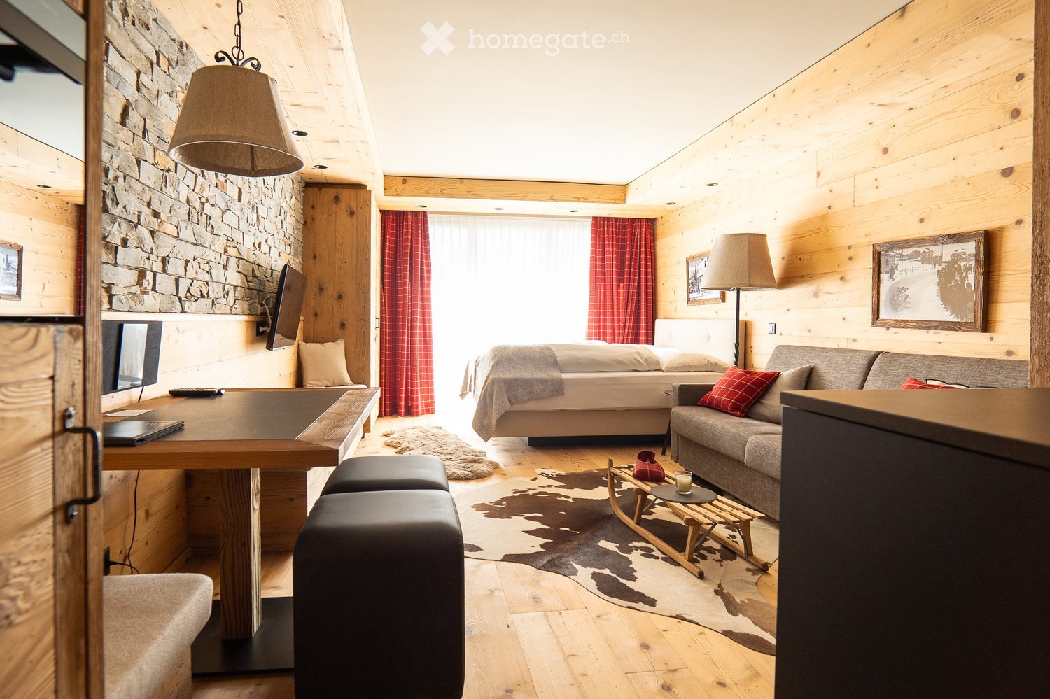 Wooden walls, wooden floor, a bed, couch, desk, monitor, lamp, picture frame, rug, coffee table