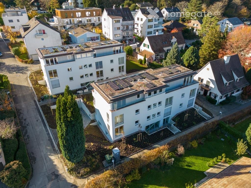 Building. Aerial view of a residential area with multiple modern houses, solar panels on rooftops, and well-maintained gardens.