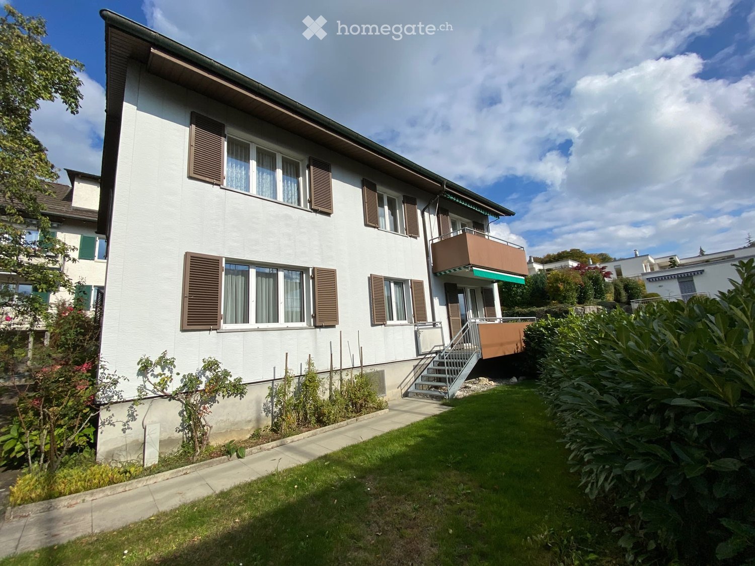 House. Two-story white house with brown shutters, a balcony, and a well-maintained garden.