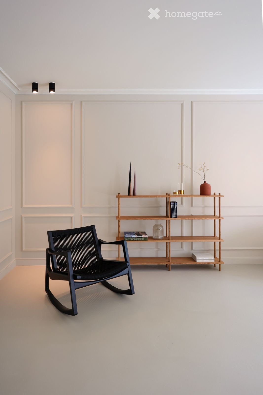 Minimalist room with white walls, black rocking chair, wooden shelf with books and decorative items