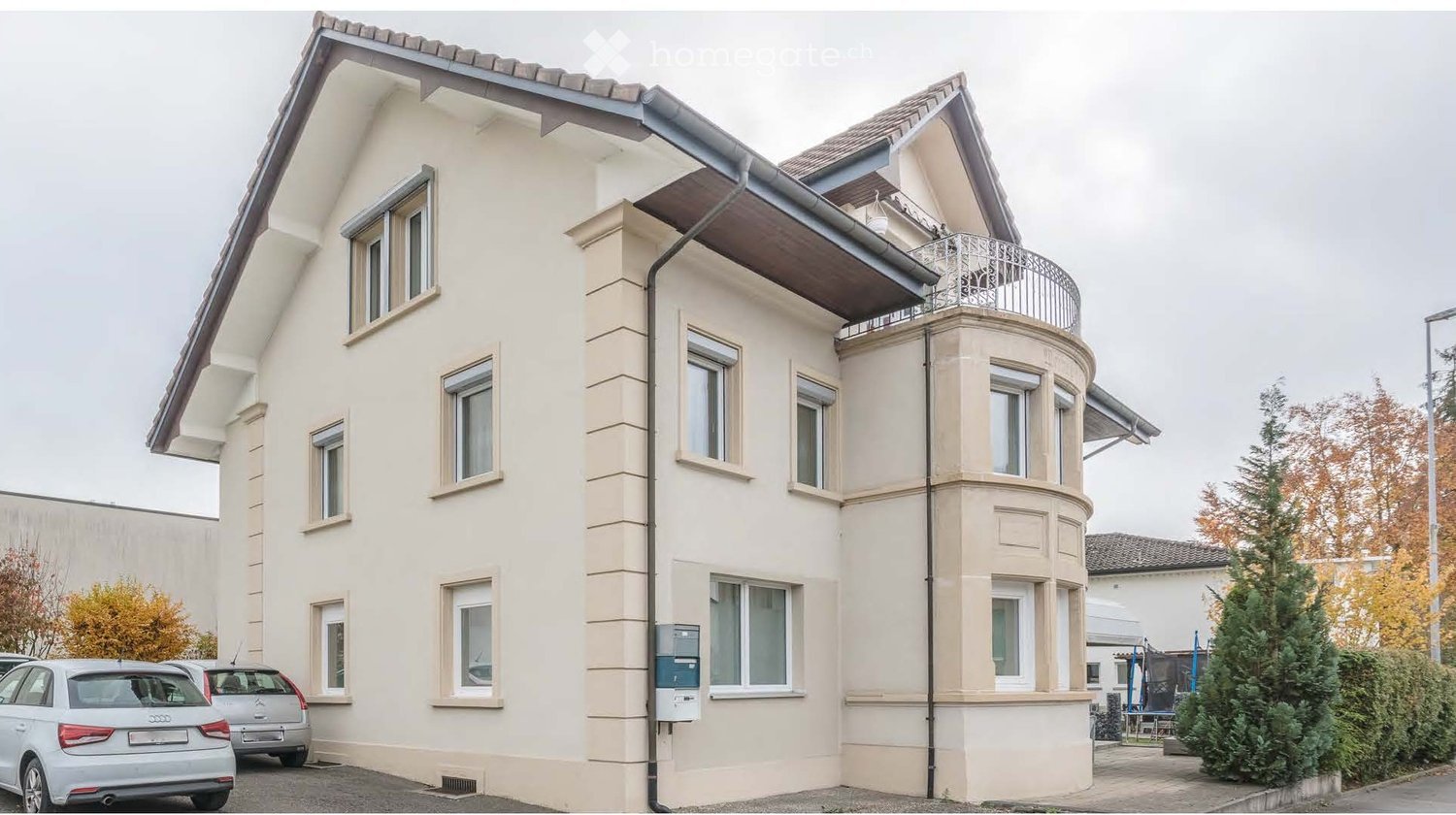 Three story house with beige walls and windows, brown roof, balcony on the second floor