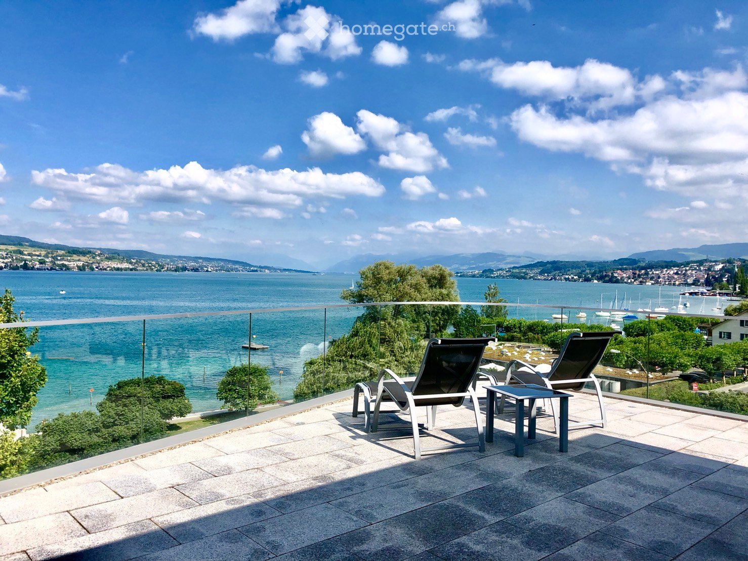 Balcony with a view of a lake, featuring two lounge chairs and a small table.