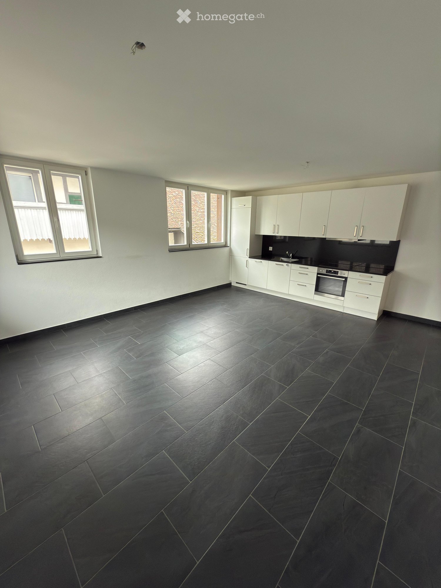 Empty kitchen with white cabinets, black countertops, and dark tiled flooring. Features a refrigerator, oven, and sink.