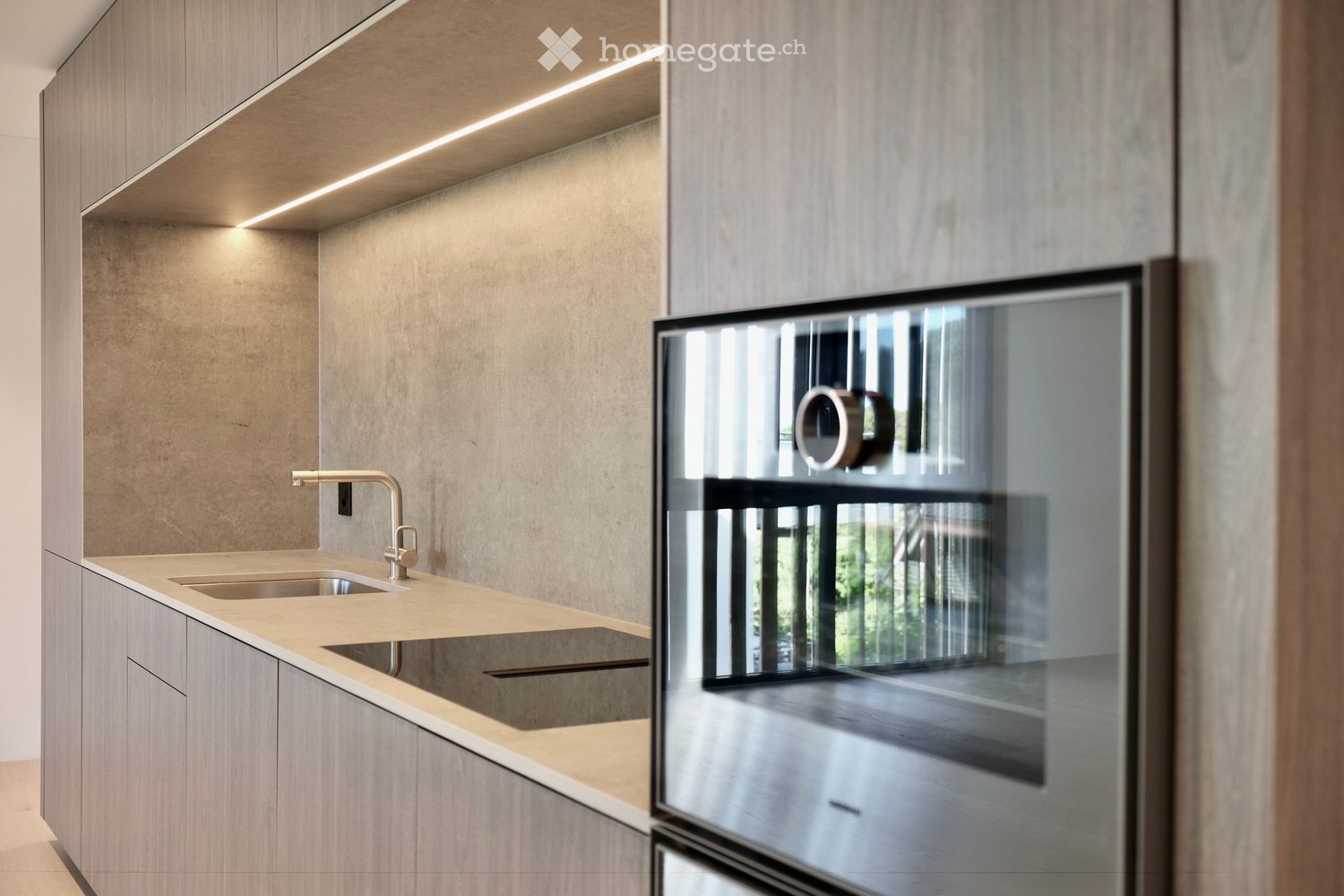 Modern kitchen with light wood cabinets, a double sink, and a sleek faucet. The space features built-in lighting and a large window offering a view of the outdoors.