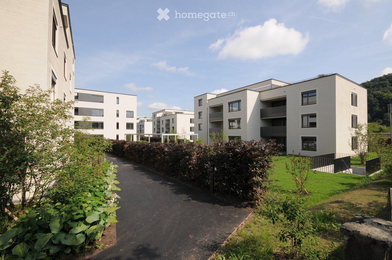 Modern residential complex with white buildings, balconies, and landscaped gardens.