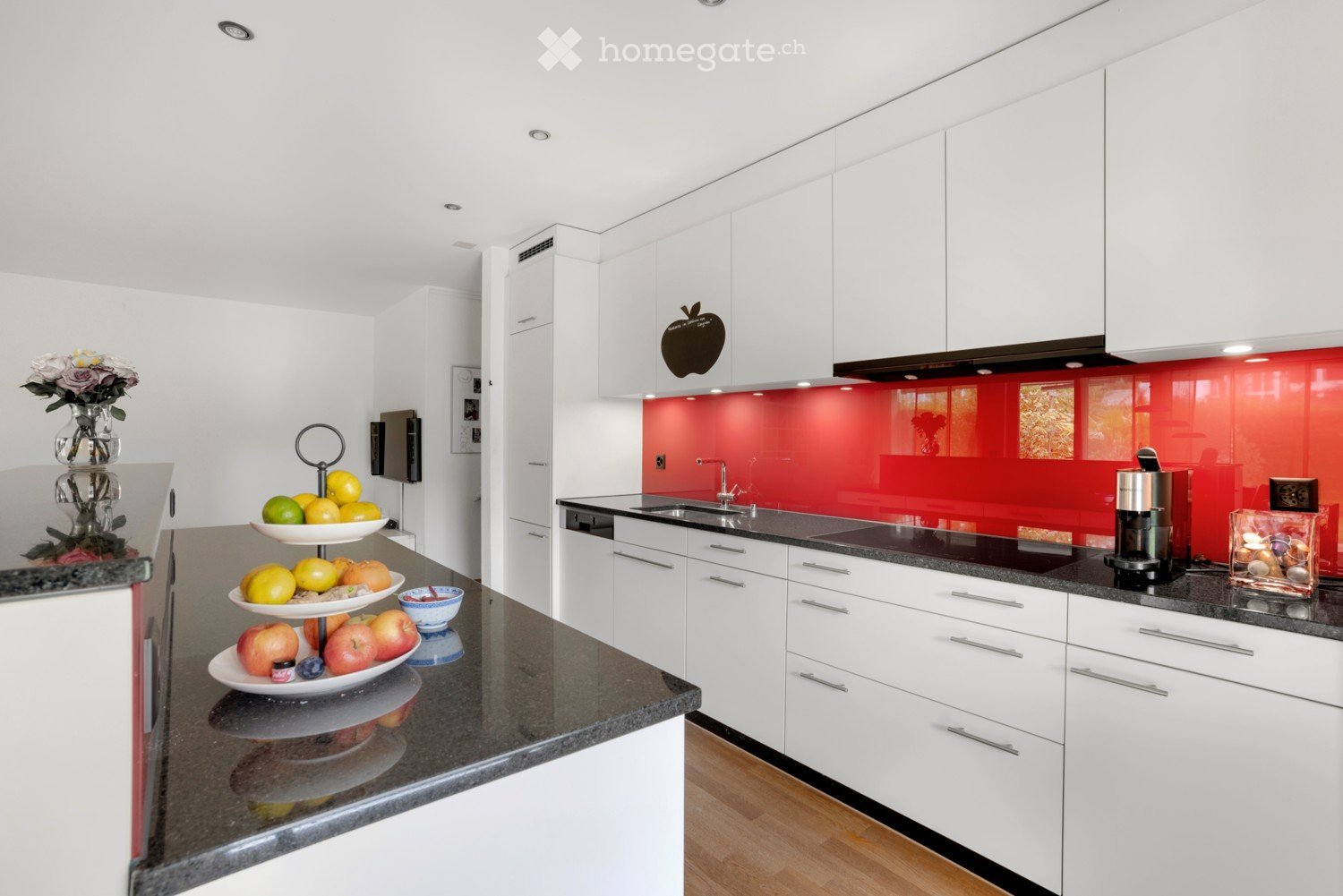 White cabinets, granite countertop, red backsplash, modern appliances, wooden floor