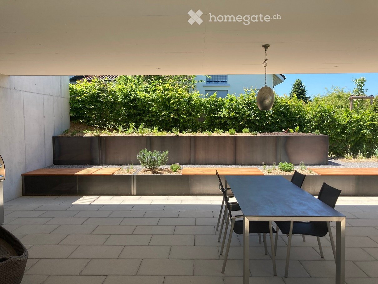 Modern outdoor patio with tiled floor, wooden benches, small plants, and a dining set including a table and chairs.