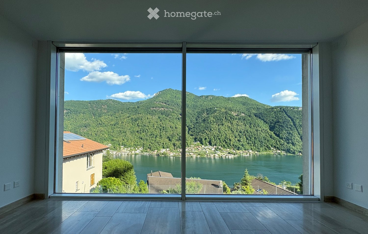 Empty room with large floor-to-ceiling windows offering a scenic view of a lake and surrounding hills.