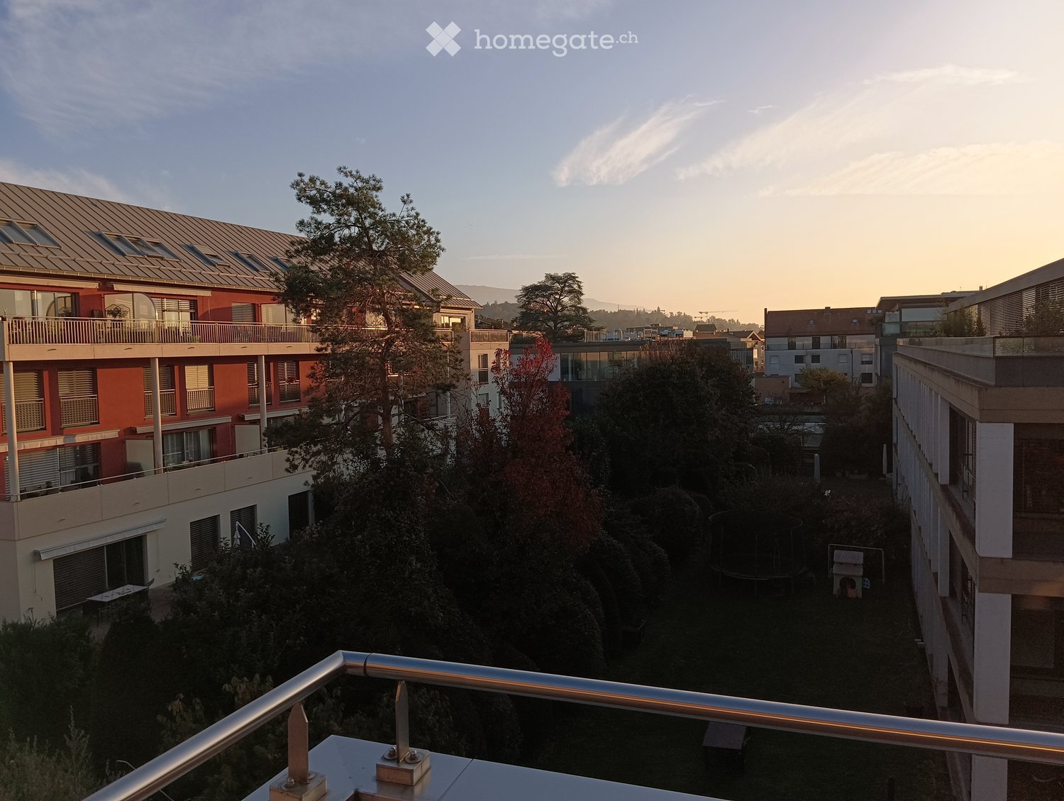 Balcony overlooking a residential area with buildings, trees, and a trampoline in the courtyard below.